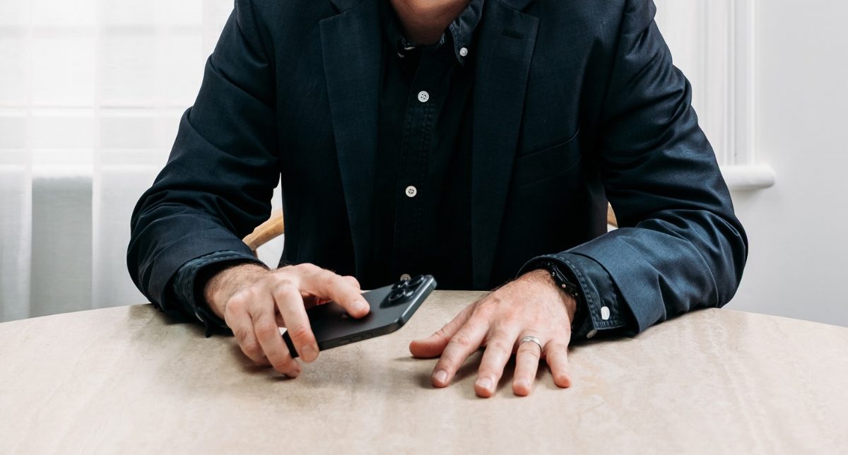 Business founder in a dark blazer seated at a table with a smartphone, ready to lead a sales conversation